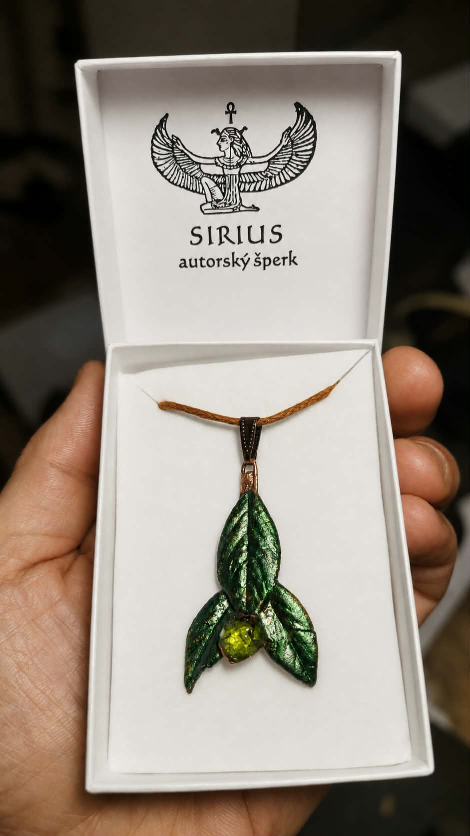 Autorský talisman Trojlist Země s českým olivínem v bílé krabičce Sirius autorský šperk držené v dlani