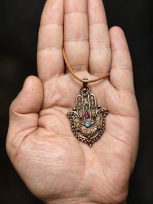 Měděný přívěsek Hamsa s měsíčním kamenem a červeným granátem na otevřené dlani.
