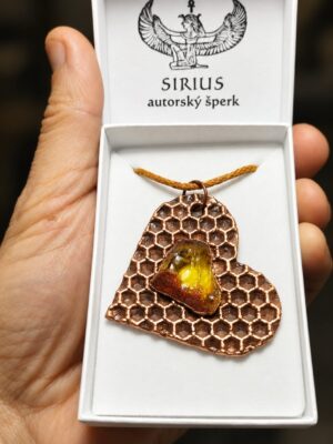 Měděný talisman z včelí plástve s baltským jantarem v bílé krabičce Sirius autorský šperk držené v dlani